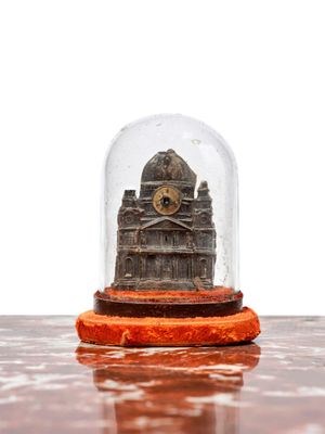 une horloge miniature placée sous un dôme en verre, posée sur une table