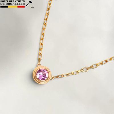 Un collier en or orné d'une pierre rose est présenté sur un fond blanc.