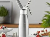 un moulin à poivre en argent posé sur un plan de travail, à côté d'une assiette de fruits