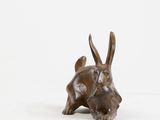 bronze sculpture of a rabbit laying down on a white surface