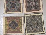 four square pieces of cloth with different designs on them on a floor