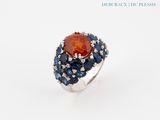 a close up of a ring with an orange stone surrounded by blue sapphires