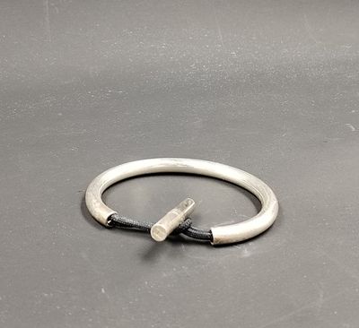 bague en argent avec un cordon noir et un fermoir en argent, posée sur un fond gris