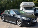 a black volvo car parked in a lot with a camper in the background