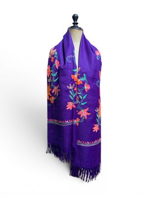 une écharpe violette ornée de fleurs colorées et de franges, posée sur un mannequin