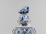 a blue and white vase with a bird on top