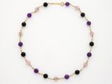 un collier composé de perles violettes et noires, monté sur une chaîne plaquée or