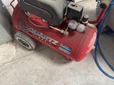 un compresseur d'air rouge posé par terre à côté d'une paire de chaussures