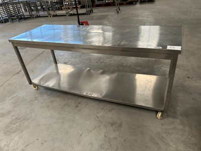 une table en acier inoxydable dans un entrepôt, avec plusieurs chaises à l'arrière-plan