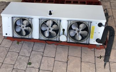 une photo d'un radiateur à trois ventilateurs posé sur un sol en briques