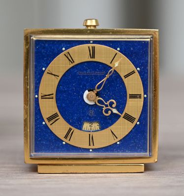une petite horloge bleue aux aiguilles dorées posée sur une table en bois