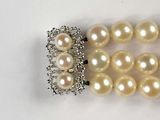 a white pearl necklace with a silver clasp on a white surface