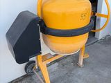 une bétonnière jaune posée sur un chariot à l'extérieur d'un bâtiment