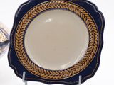 a blue and gold plate sitting on a stand next to a vase