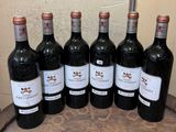 six bottles of red wine are lined up on a wooden barrel
