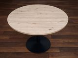 une petite table ronde avec un piètement noir posée sur un parquet