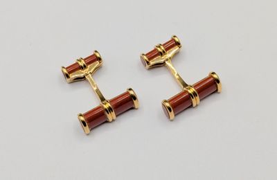 a pair of gold and red cufflinks on a white background