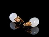 une paire de boucles d'oreilles blanches et dorées posées sur un fond noir