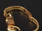 a gold bracelet with a clasp on a black background