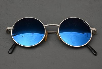 lunettes de soleil argentées aux verres bleus, posées sur une surface grise