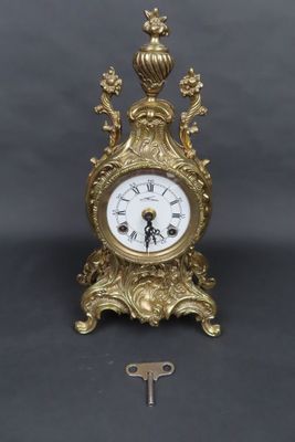 une horloge en or posée sur une table à côté d'une clé