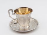 une tasse et une soucoupe anciennes en argent, posées sur une soucoupe, sur une surface blanche