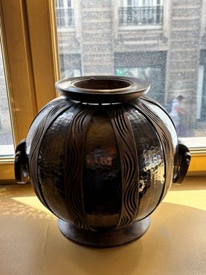 un vase noir posé sur une table devant une fenêtre