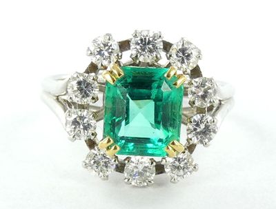 un gros plan d'une bague sertie d'une émeraude verte et de diamants, posée sur une surface blanche
