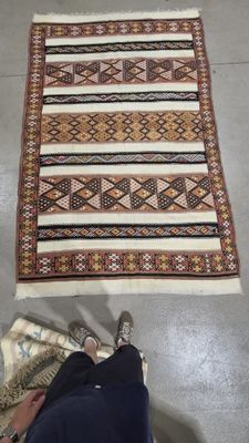 Quelqu'un est assis par terre, à côté d'un tapis et d'une paire de chaussures.