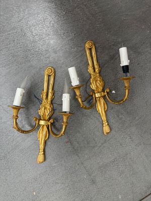 trois appliques dorées avec des bougies blanches posées sur un support gris
