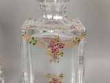 une petite bouteille en verre ornée d'un motif floral, à côté d'une autre bouteille en verre, plus petite, également ornée d'un motif floral