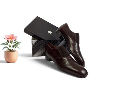 une paire de chaussures en cuir marron pour homme, à côté d'une boîte ornée d'une fleur