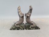 une paire d'otaries en bronze posées sur des socles en marbre, sur fond gris