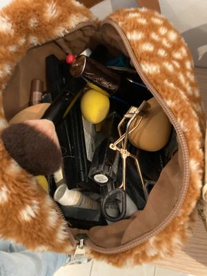 un sac à main rempli de maquillage et d'autres objets, posé par terre
