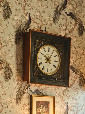une horloge accrochée au mur au-dessus d'un tableau représentant des oiseaux