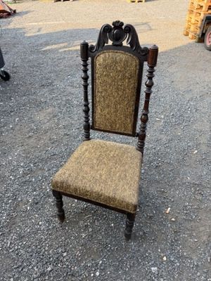 Une vieille chaise dont l'assise est recouverte d'un tissu marron se trouve sur un parking