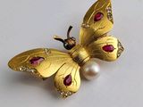 une image représentant une broche en forme de papillon en or ornée de perles, sur un fond blanc
