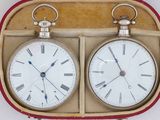 two clocks sitting in a case on a white surface