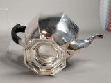a silver teapot sitting on a table next to a glass