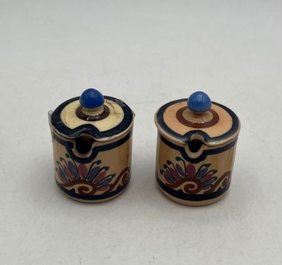 Deux petits récipients en céramique avec des couvercles bleus sont posés sur une surface blanche.