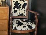 une chaise à motif vache à côté d'une commode sur laquelle est posée une lampe