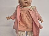 a small doll with a pink dress and bonnet on a stand