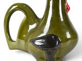 a green vase with a bird on it on a white surface