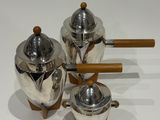 three silver teapots with wooden handles on a white surface