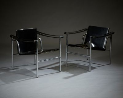 une paire de fauteuils en cuir noir dans une pièce sombre, avec une lampe posée au sol