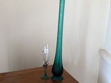 un vase en verre vert posé sur une table en bois à côté d'un tableau