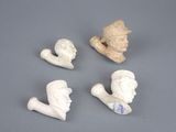 three small sculptures of heads and a pipe on a gray surface