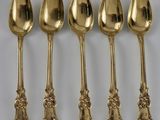 cinq cuillères en or aux motifs ouvragés sont alignées sur une surface blanche