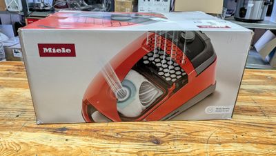 une machine à écrire rouge et noire dans une boîte posée sur une table en bois