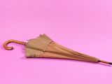 un parapluie marron avec un manche en bois sur fond rose